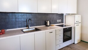 A modern kitchen with white cabinets, a black tiled backsplash, a sink, a kettle, and a refrigerator. - N256 - Numana, brand new three-room apartment with garden (Sirolo)