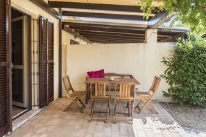 An outdoor patio with a wooden table and chairs, a concrete wall, and a metal gate.