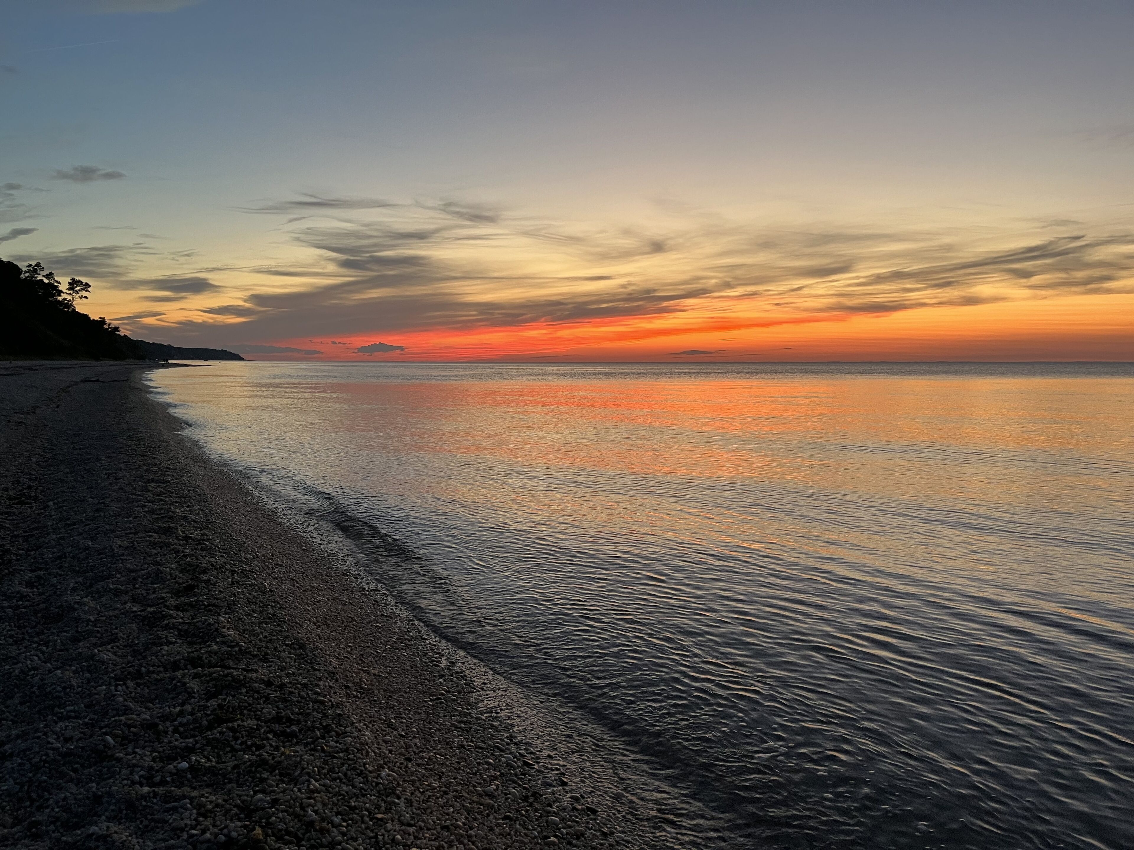 A beach with a calm sea and a sunset.