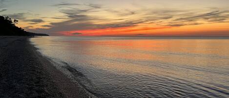 A beach with a calm sea and a sunset.