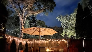 Eine Terrasse im Freien mit Holzzaun, Lichterkette, Tisch und Stühlen sowie Sonnenschirm.