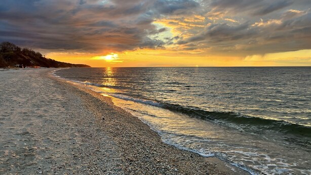 Ein Strand mit Sonnenuntergang, ruhiger See und felsiger Küste.
