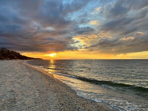 A beach with a sunset, calm sea, and a rocky shoreline.