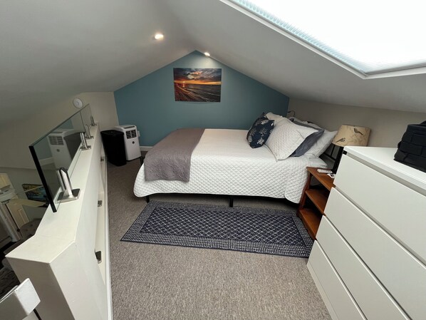 A bedroom with a bed, a desk, a chair, a window, and a ceiling fan.
