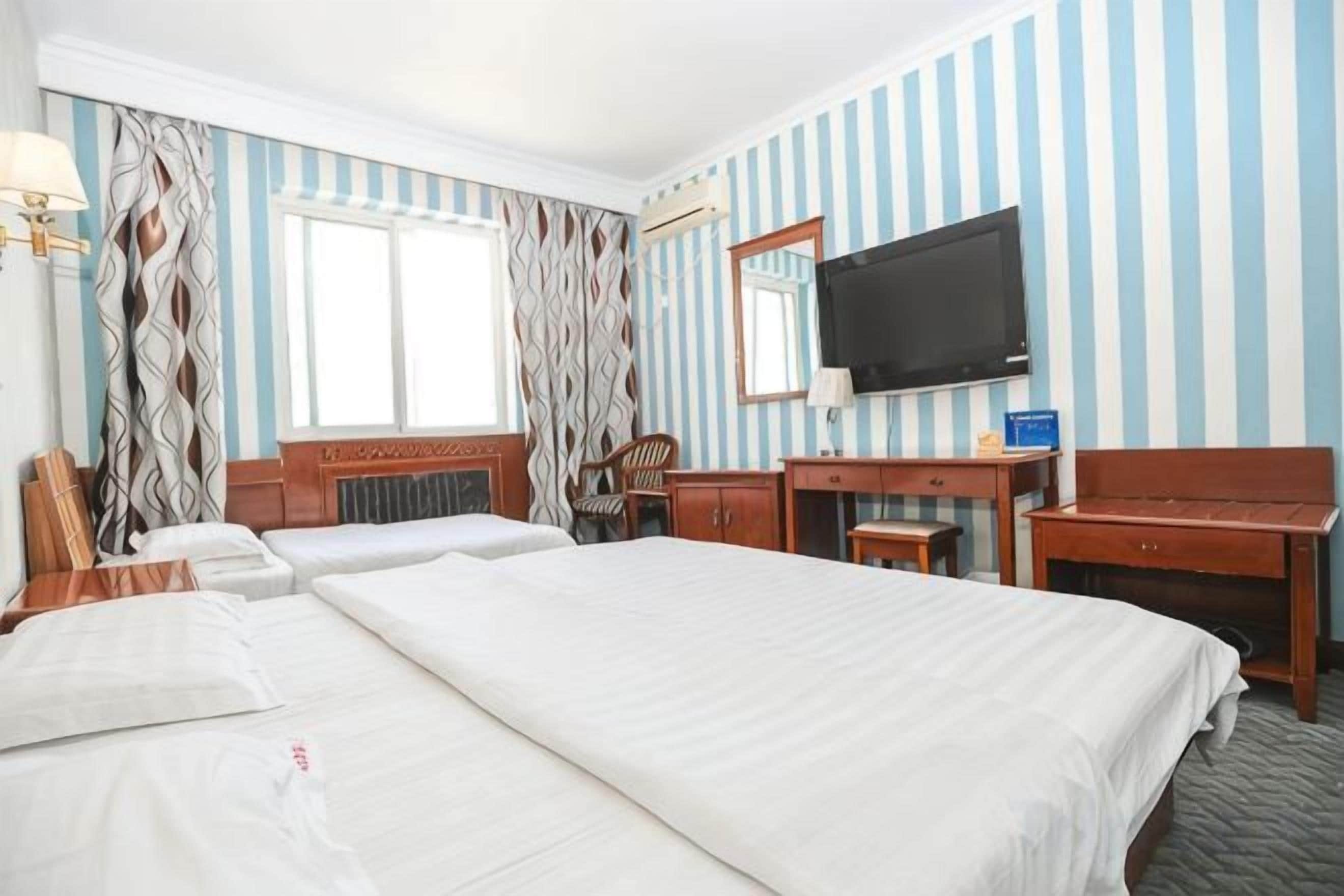 A hotel room with two beds, a television, a desk, and a mirror.