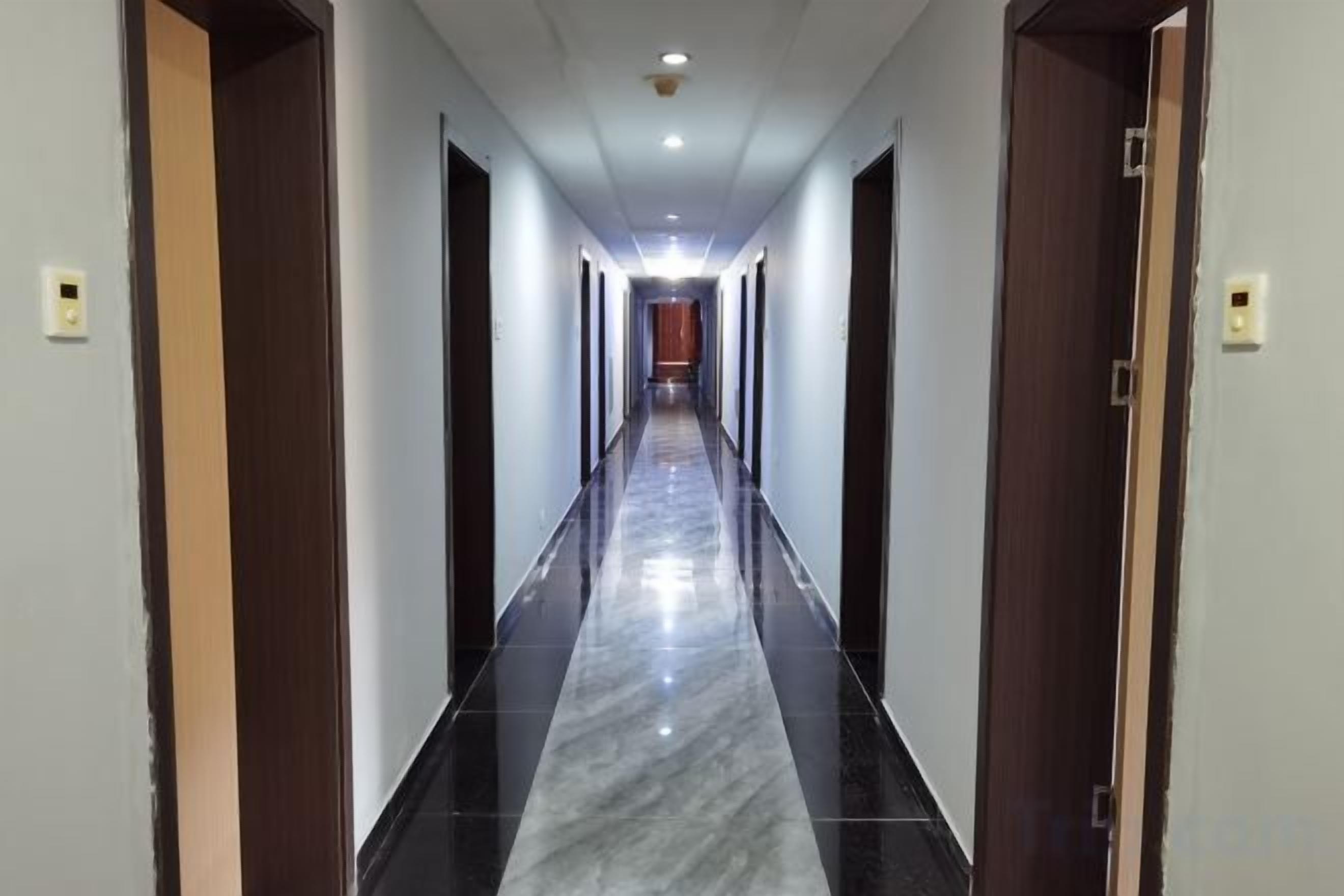 Un pasillo de hotel con suelo de mármol, puertas de madera y una lámpara en el techo.