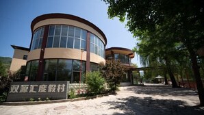 A modern building with a curved facade, large windows, and a stone-paved entrance. - Shuangyuanhui Resort (Beijing)