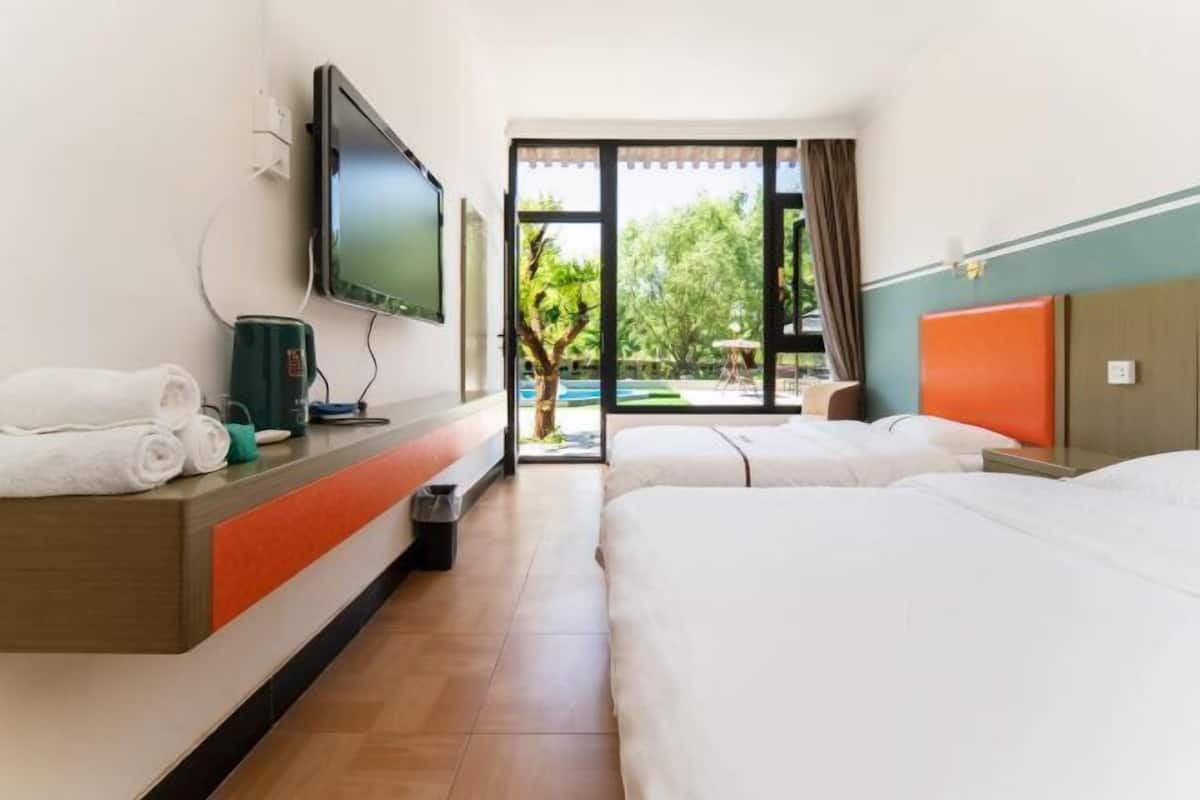 Ein Hotelzimmer mit zwei Betten, einem Fernseher, einem Schreibtisch mit Kaffeemaschine und Blick auf Pool und Grünflächen.