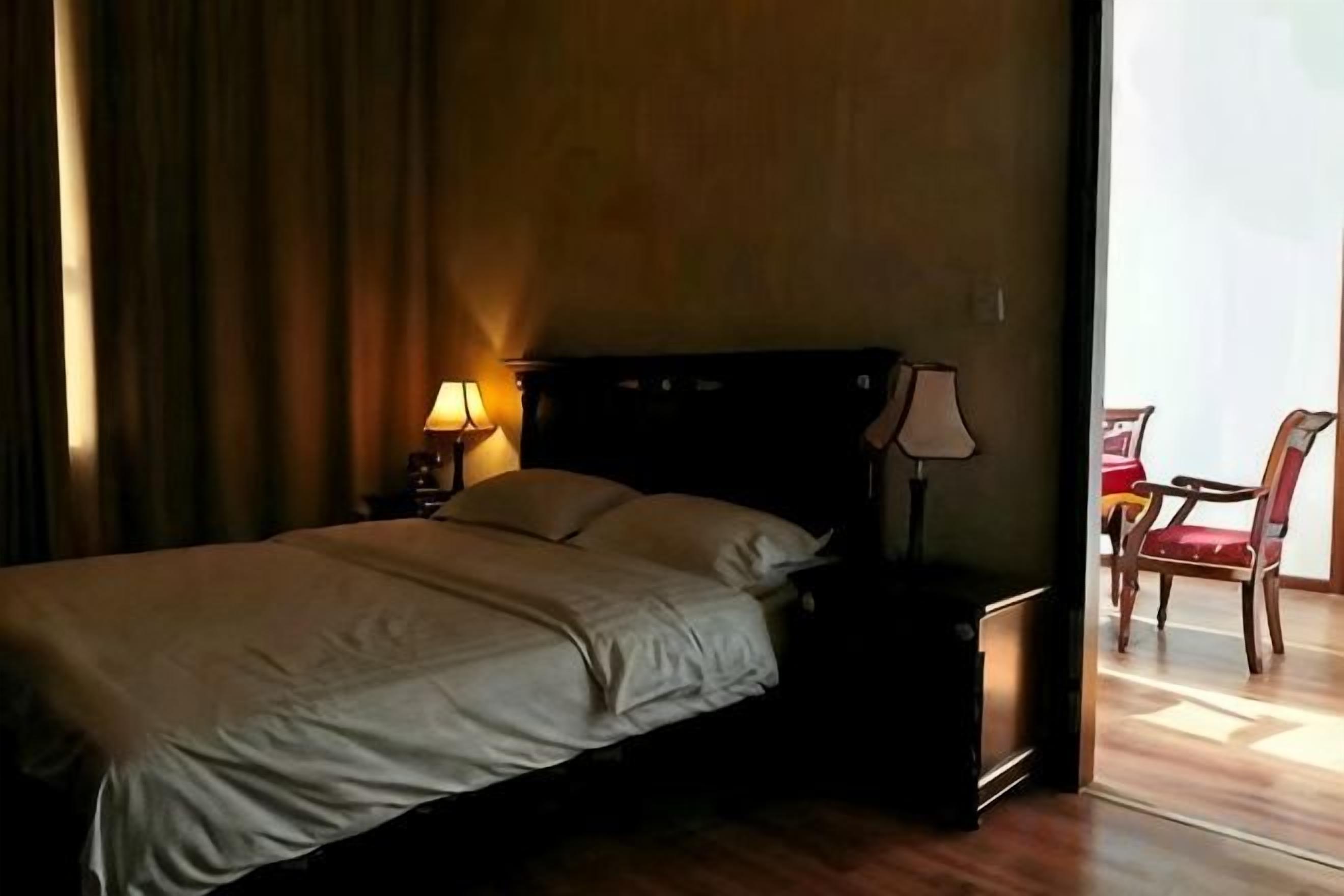 A hotel room with a bed, bedside lamps, a chair, and a view of the outside.