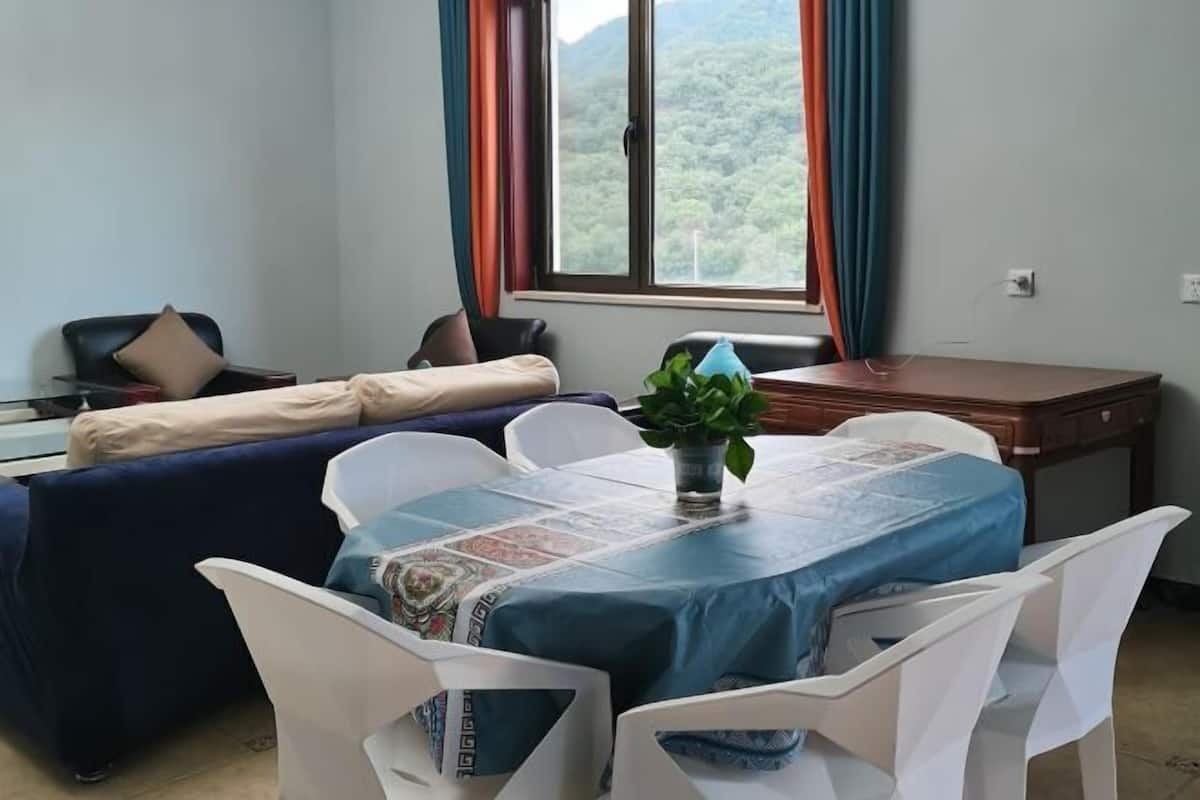 Ein Zimmer mit einem Bett, einem Schreibtisch, einem Tisch mit Stühlen, einem Fenster mit Vorhängen und einer Pflanze auf dem Tisch.