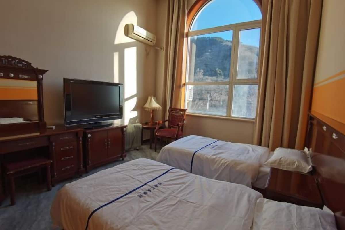 Ein Hotelzimmer mit zwei Betten, einem Fernseher, einem Schreibtisch und einem Fenster mit Blick auf die Berge.