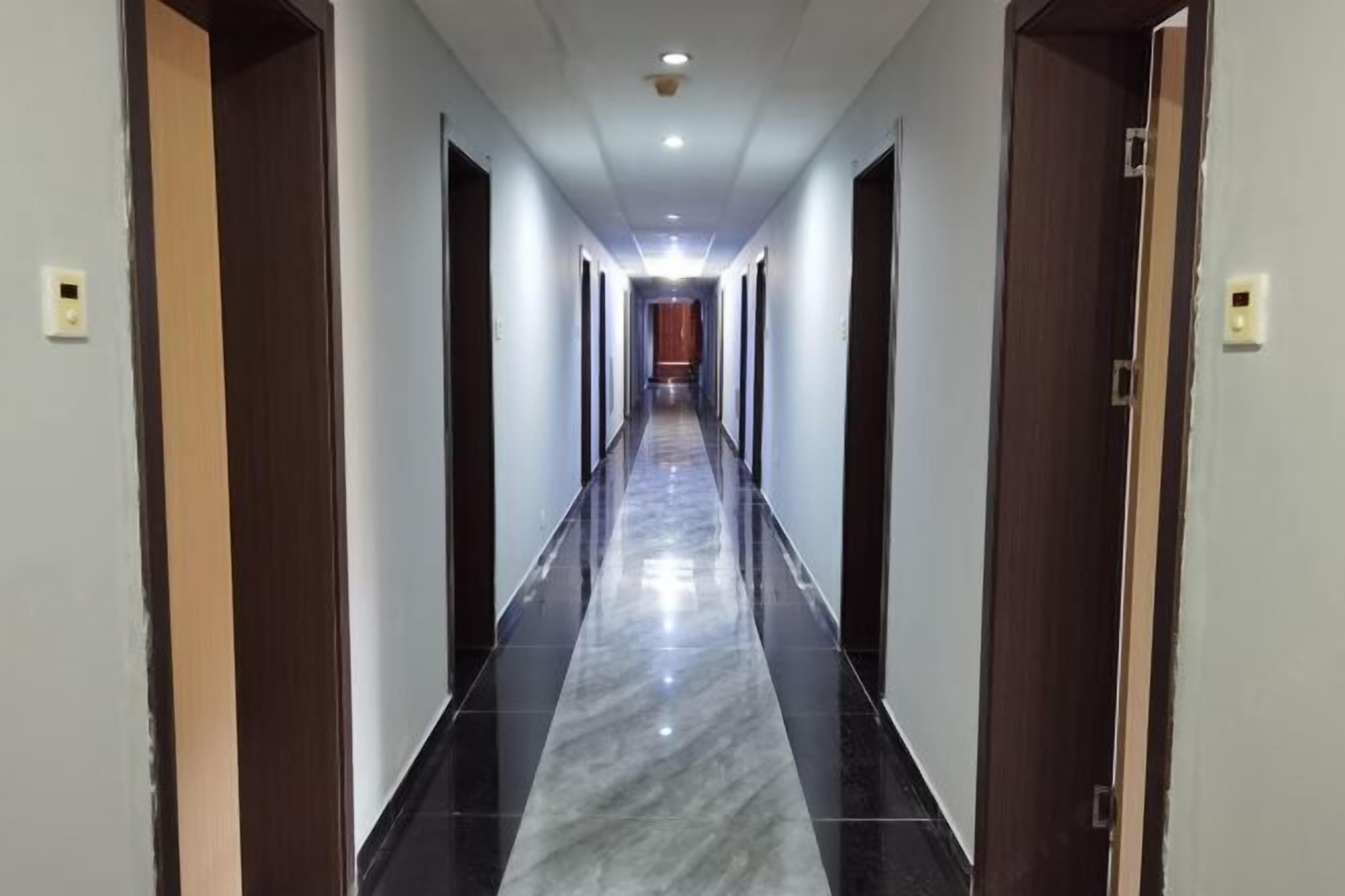 A long, narrow hallway with a shiny black and white marble floor, flanked by wooden doors on both sides.