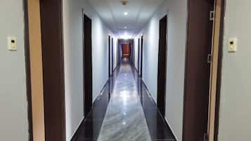 A long, narrow hallway with a shiny black and white marble floor, flanked by wooden doors on both sides.