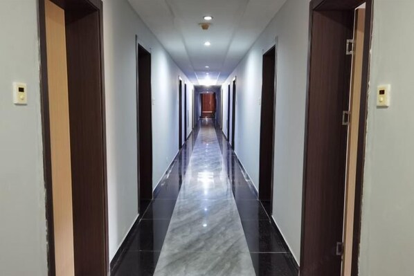 A long, narrow hallway with a shiny black and white marble floor, flanked by wooden doors on both sides.