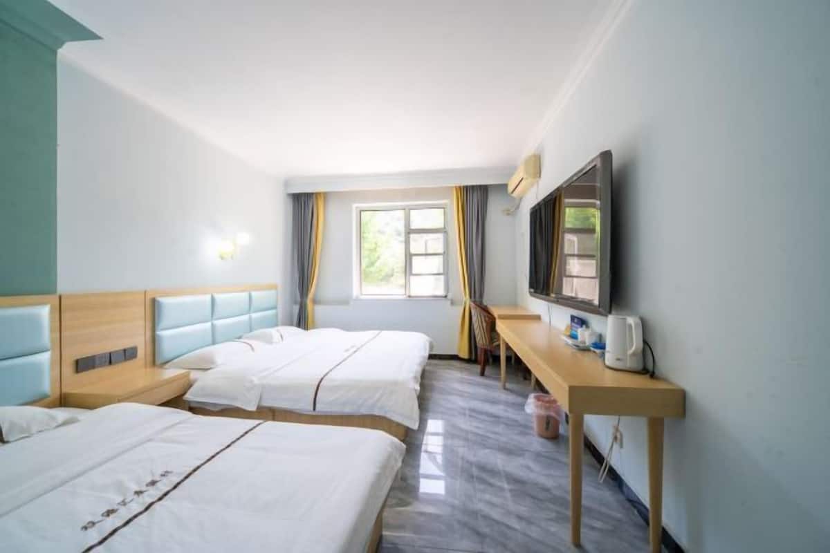 Ein Hotelzimmer mit zwei Betten, einem Schreibtisch, einem Fernseher und einem Fenster mit Vorhängen.