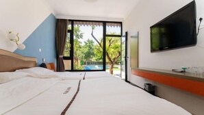 A hotel room with a bed, a TV, a window with a view of trees and a pool, and a trash bin. - Shuangyuanhui Resort (Beijing)