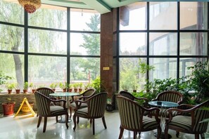A room with large windows, a table with chairs, and potted plants. - Shuangyuanhui Resort (Beijing)