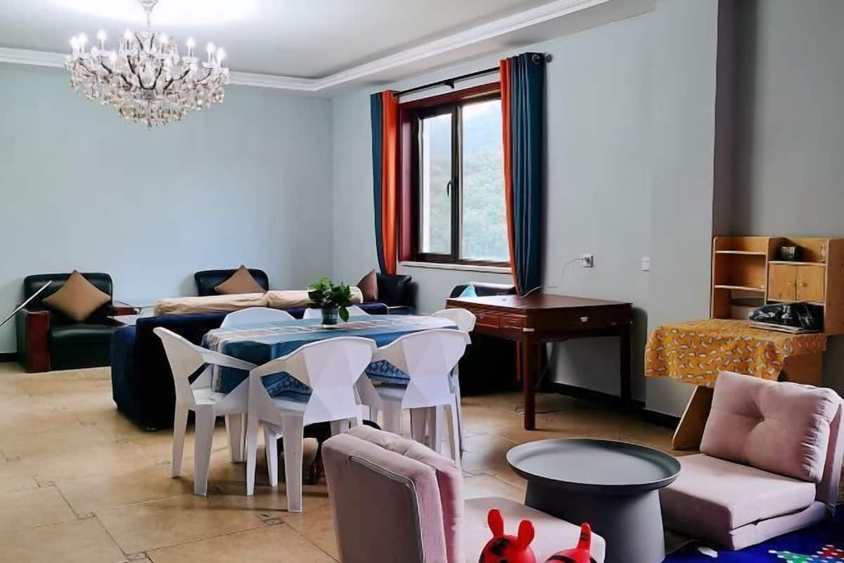 Ein Wohnzimmer mit Essbereich, einer Kristallleuchtre, einem Fenster mit Vorhängen und einem kleinen Tisch mit Pflanze.