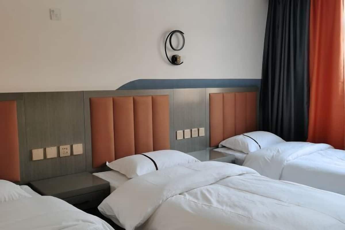 Ein Hotelzimmer mit drei Betten, einem Kopfteil mit kreisförmigem Design und einer wandmontierten Lampe.