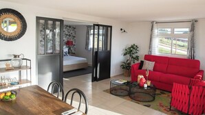 A living room with a red sofa, a dining table with chairs, a kitchen area with a fridge, and a bedroom with a bed and curtains.