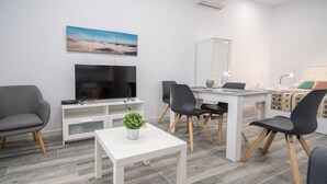 Un soggiorno moderno con TV a schermo piatto, un tavolo da pranzo con sedie, un divano grigio e un piccolo tavolino bianco con una pianta.