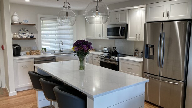 A modern kitchen with white cabinetry, stainless steel appliances, and a central island with bar stools. - Lake Winnipesaukee Townhouse (Gilford)