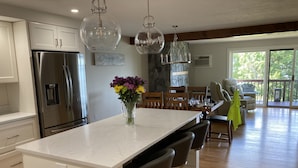 A modern kitchen with a large island, stainless steel appliances, and a dining area with a view. - Lake Winnipesaukee Townhouse (Gilford)