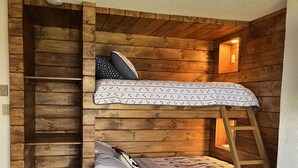 A bunk bed with a ladder, wooden walls, and a small window with a light. - Lake Winnipesaukee Townhouse (Gilford)