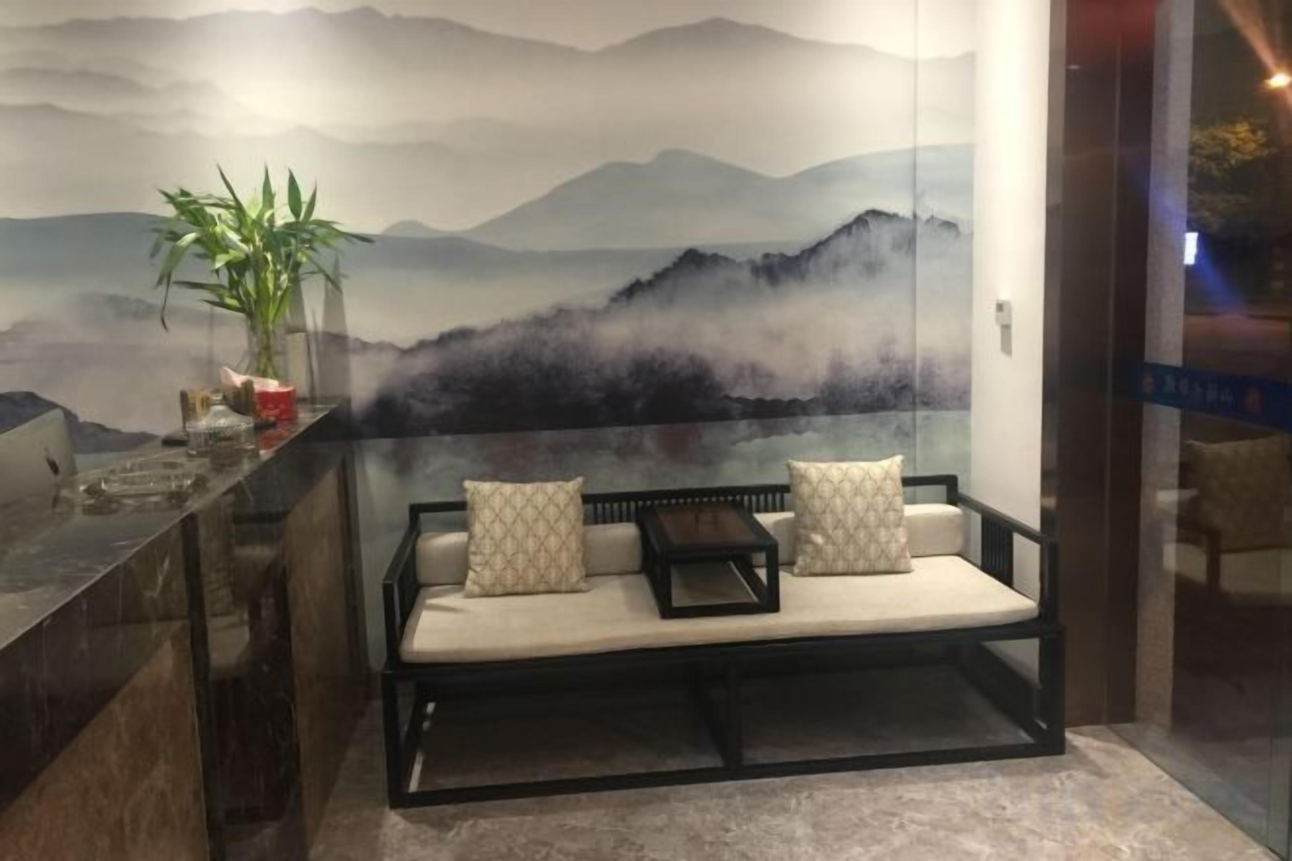 A seating area with a sofa and cushions, a potted plant, and a wall with a mountain landscape mural.