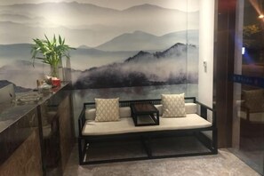 A seating area with a sofa and cushions, a potted plant, and a wall with a mountain landscape mural. - Shanyushui Post Inn (Nantong)