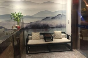 Un área de estar con sofá y cojines, una planta en maceta y una pared con un mural de paisaje montañoso.