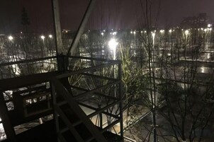 Vista nocturna de una obra en construcción con andamios metálicos y árboles desprovistos de hojas.
