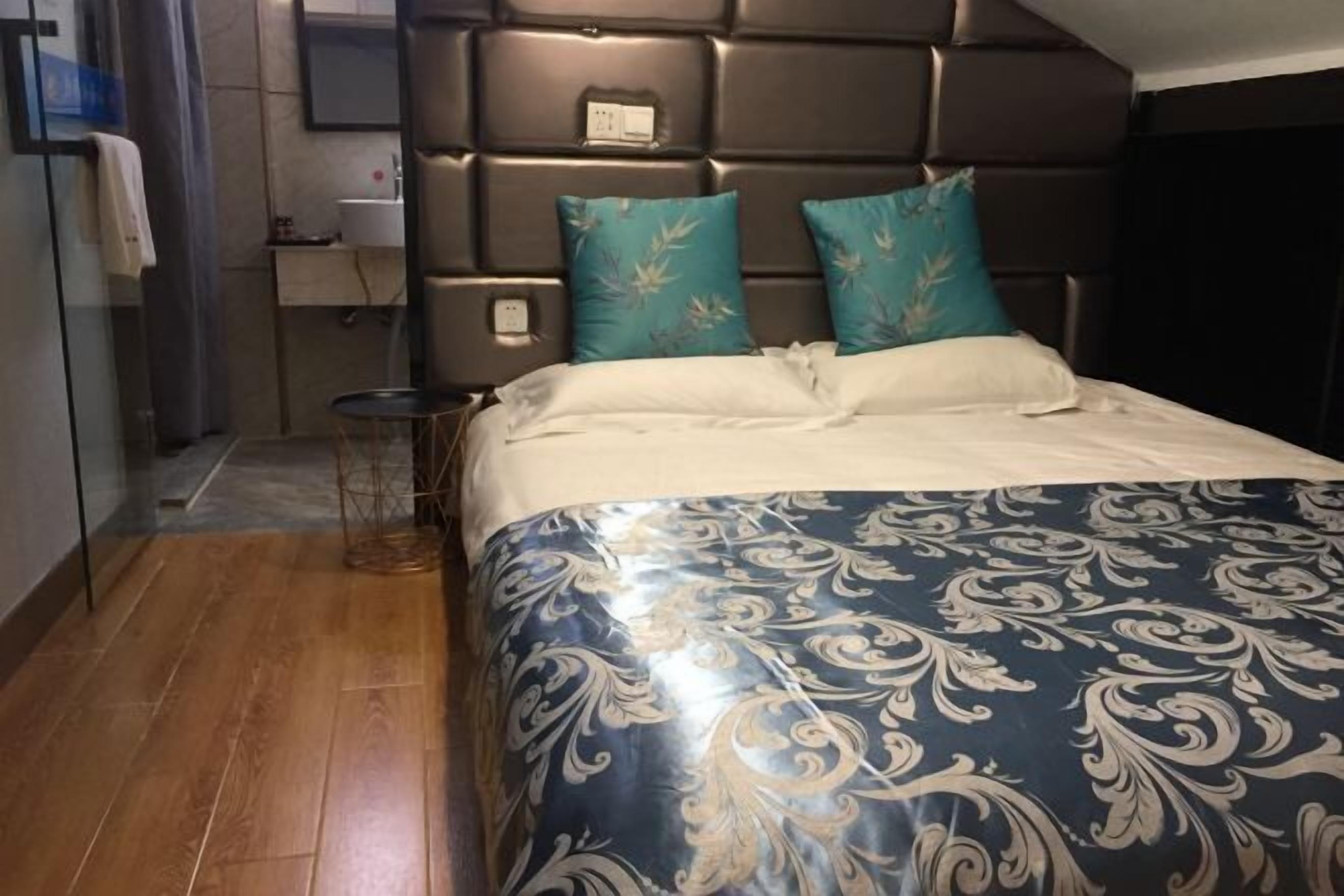 A bedroom with a dark headboard, a bed with a patterned bedspread, and a small bedside table.