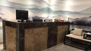 Bancada de recepção com monitor de computador, laptop e máquina de café. Há uma cadeira com almofada e um mural na parede retratando montanhas e nuvens.