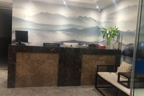 A reception desk with a computer, a plant, and a seating area with a bench. - Shanyushui Post Inn (Nantong)