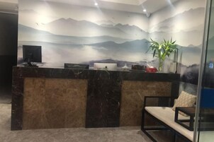 Una recepción con una computadora, una planta y una zona de estar con un banco.