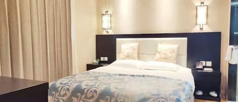A hotel room with a large bed, two bedside tables, a headboard, and two wall-mounted lamps.