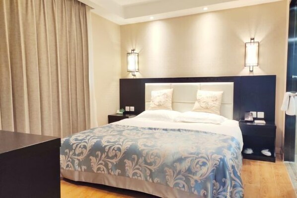 Quarto de hotel com uma cama grande, duas mesas de cabeceira, uma cabeceira e duas luminárias fixadas na parede.