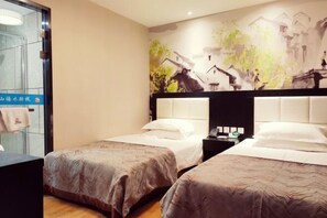 Quarto de hotel com duas camas, uma mesinha de cabeceira, um mural na parede e uma porta de vidro com uma toalha pendurada.
