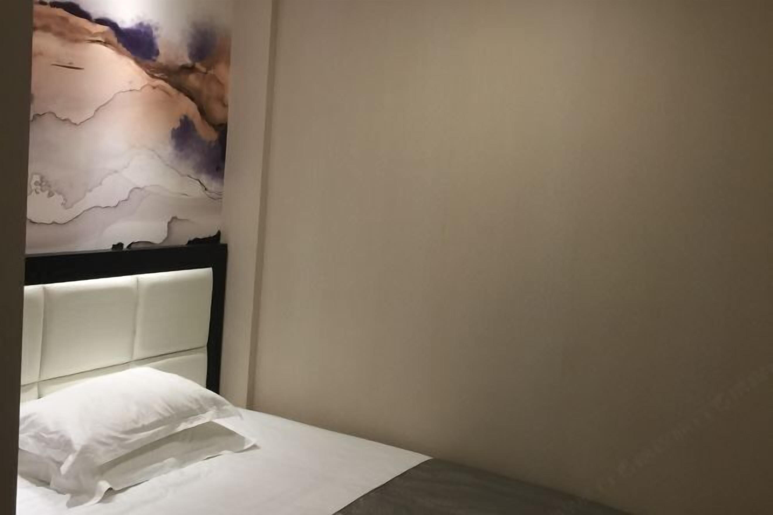 A hotel room with a bed, a headboard, and a wall with a painting.