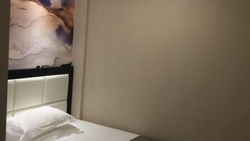 A hotel room with a bed, a headboard, and a wall with a painting.