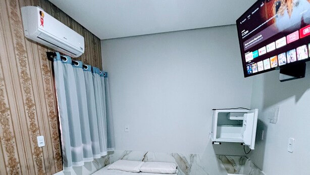 Ein Hotelzimmer mit einem Bett, einem an der Wand befestigten Fernseher, einer Klimaanlage und einem kleinen Tisch.