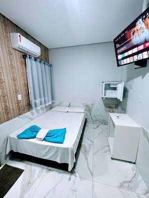 A hotel room with a bed, a TV mounted on the wall, an air conditioner, and a small table. - Entre Rios Hotel (Paraiso Do Tocantins)