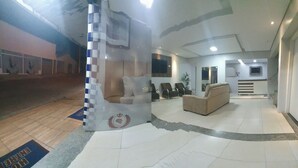 Eine Hotelhalle mit Empfangsschalter, Sitzgelegenheiten und einer Treppe zu den oberen Stockwerken.