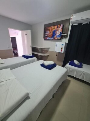Habitació d'hotel amb tres llits individuals, un televisor de pantalla plana fixat a la paret, una petita estant amb un comandament a distància i una porta que dona a una altra habitació.