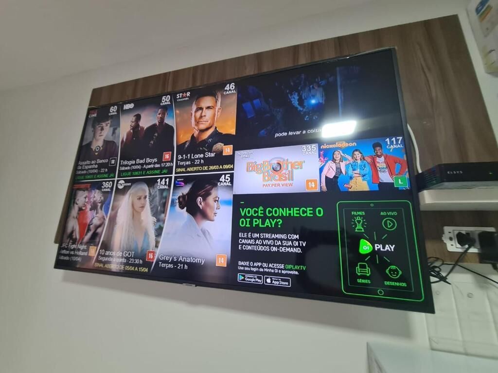 Um ecrã digital a exibir vários canais de televisão e um anúncio promocional de um serviço de streaming.