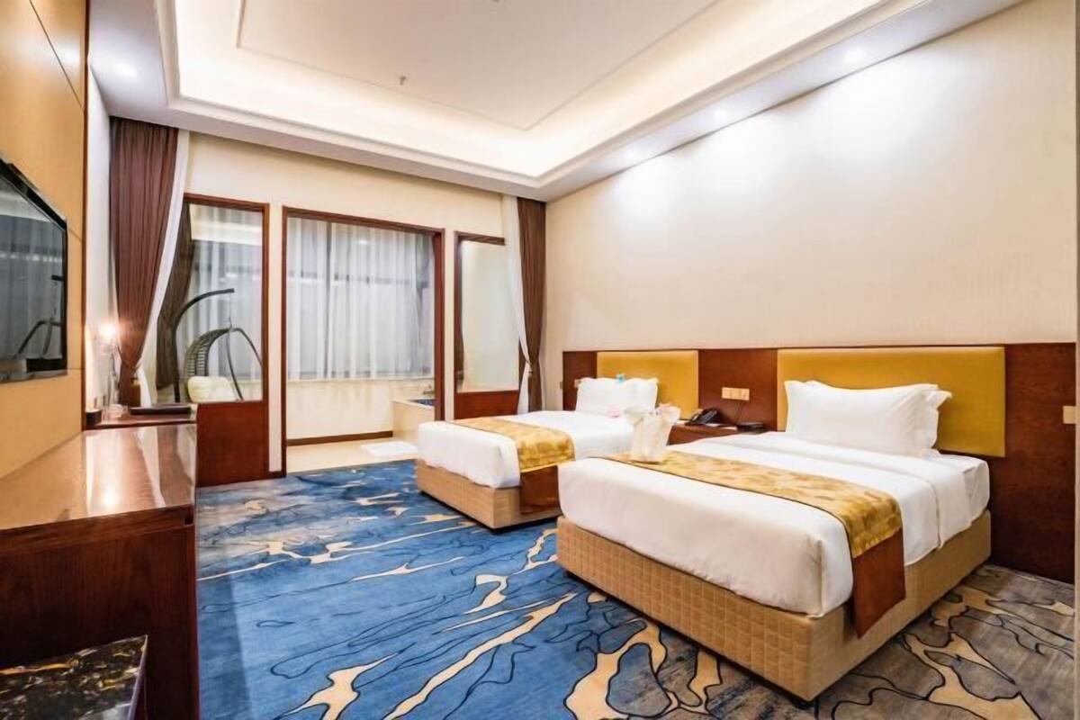 A hotel room with two beds, a desk, a chair, and a large window with curtains.