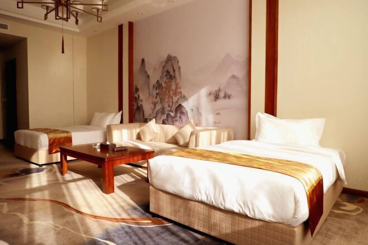 A hotel room with a bed, two sofas, a coffee table, and a large wall painting.