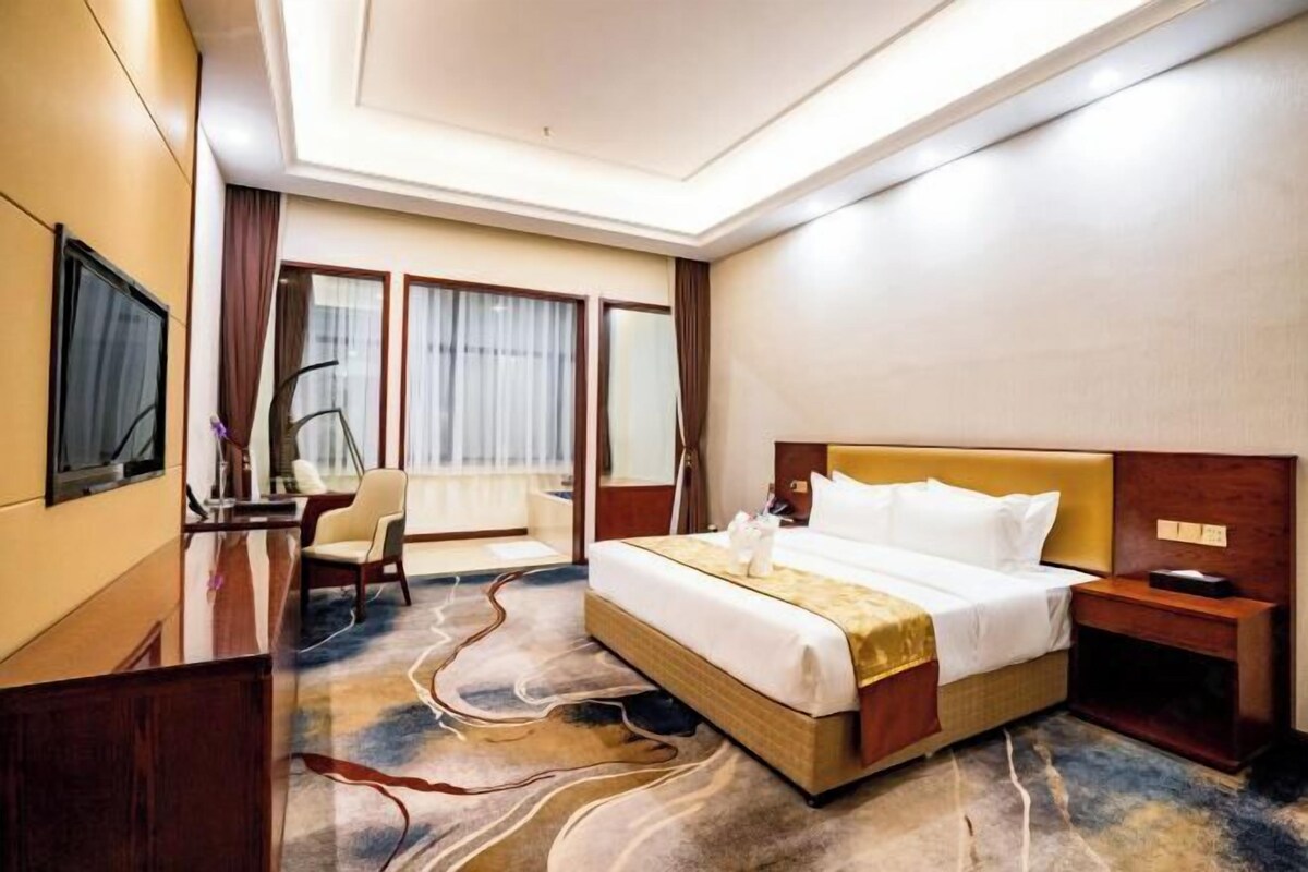 A hotel room with a large bed, a desk, a chair, and a television.