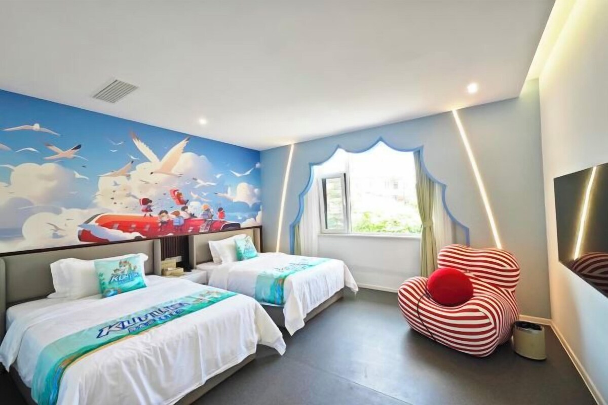 A hotel room with two beds, a mural on the wall, a window with curtains, and a red chair.